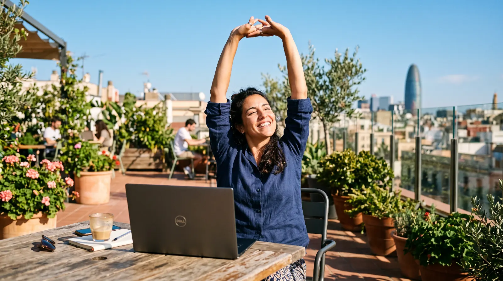 Mujer estirándose feliz mientras trabaja con su portátil en una terraza